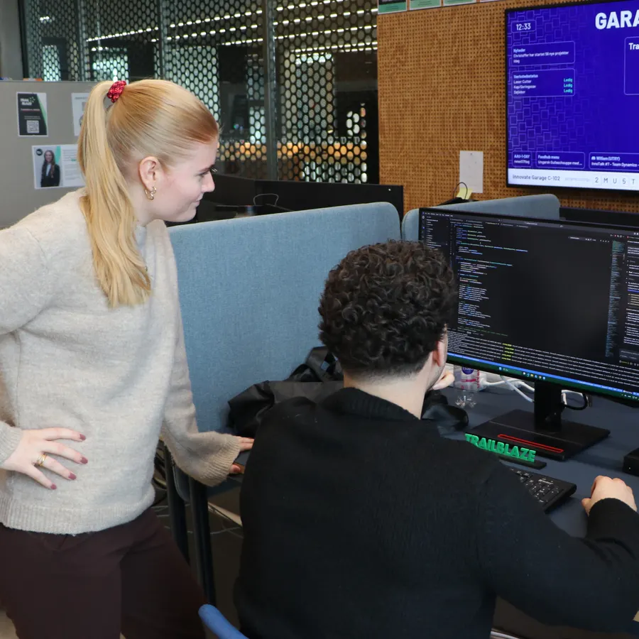 Two students at a computer with code on the screen