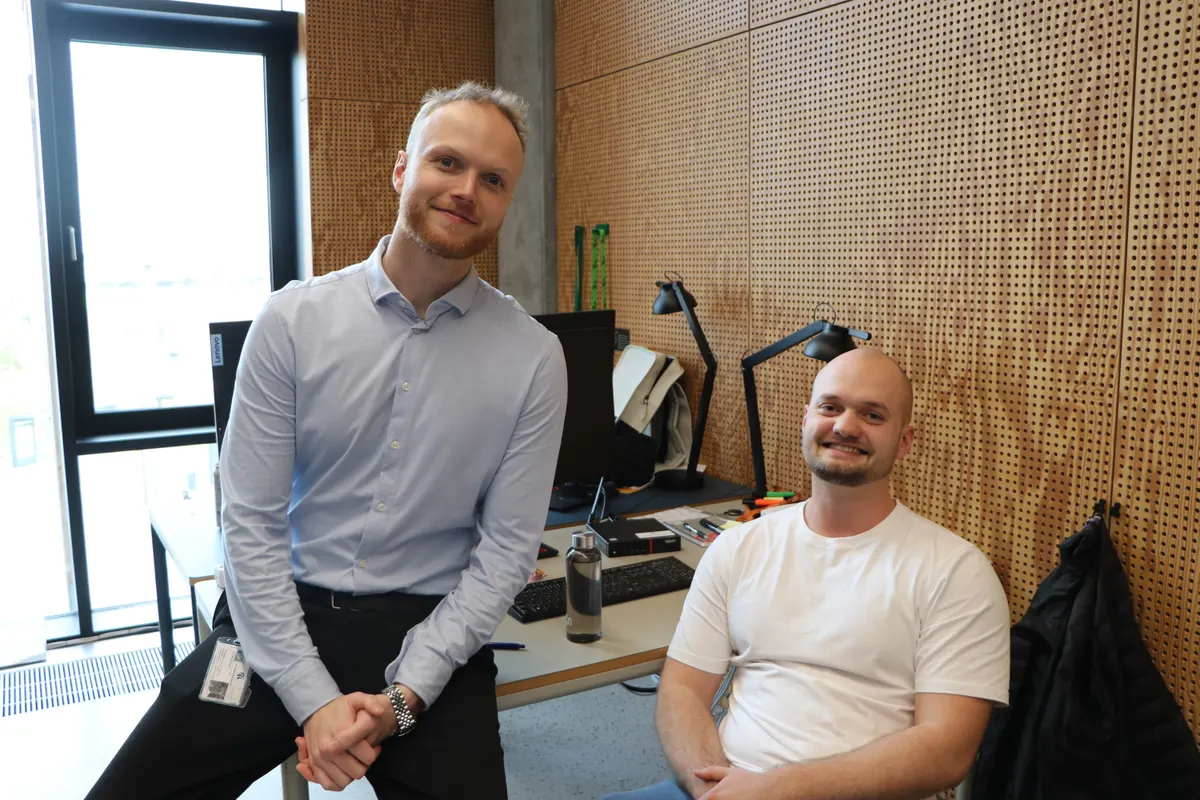 Two smiling men at a desk in an office with wooden panels
