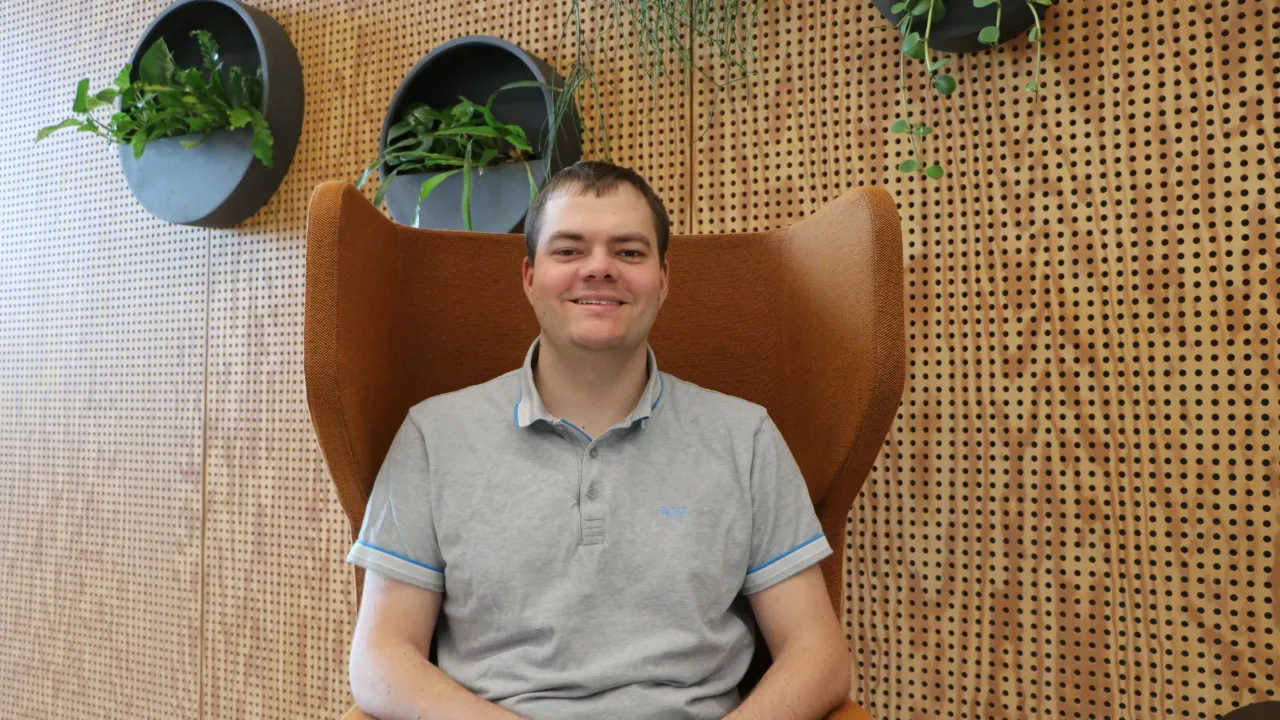 Smiling student in an armchair in front of a wooden wall with plants