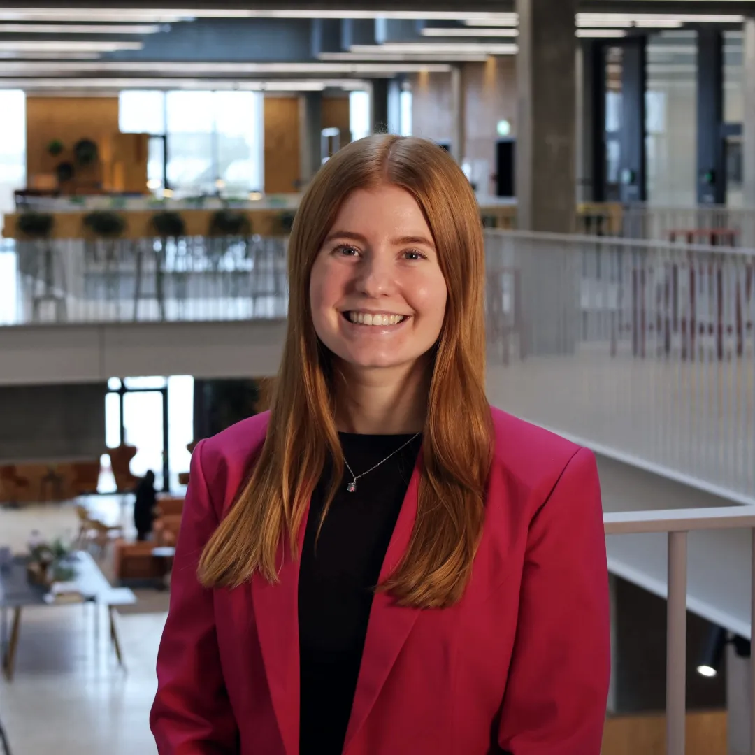 Smiling woman in a pink blazer in a bright university building