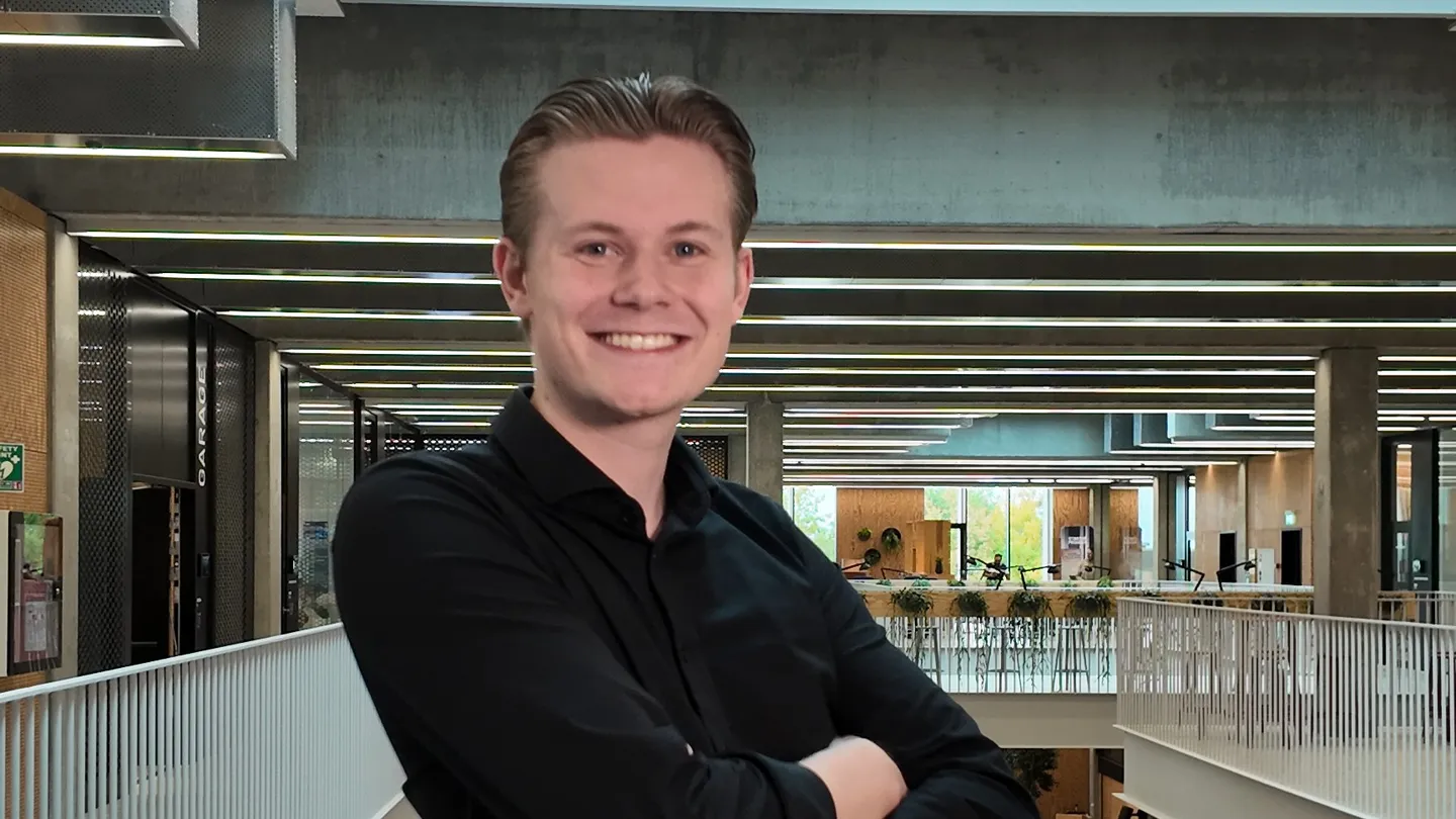 Smiling student in a black shirt with arms crossed in a bright university building