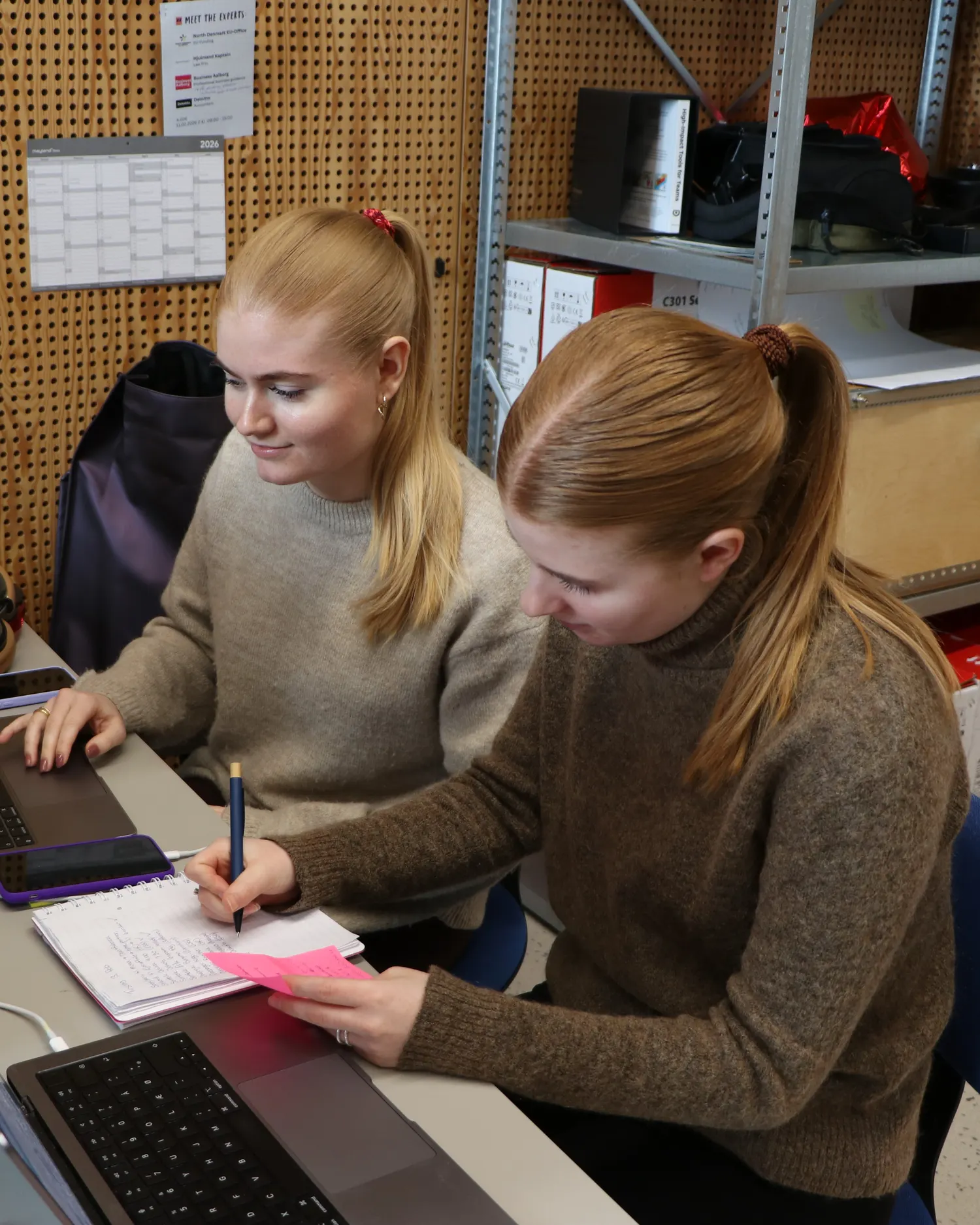 Two people from TrailBlaze working together at a desk with laptops and a notebook