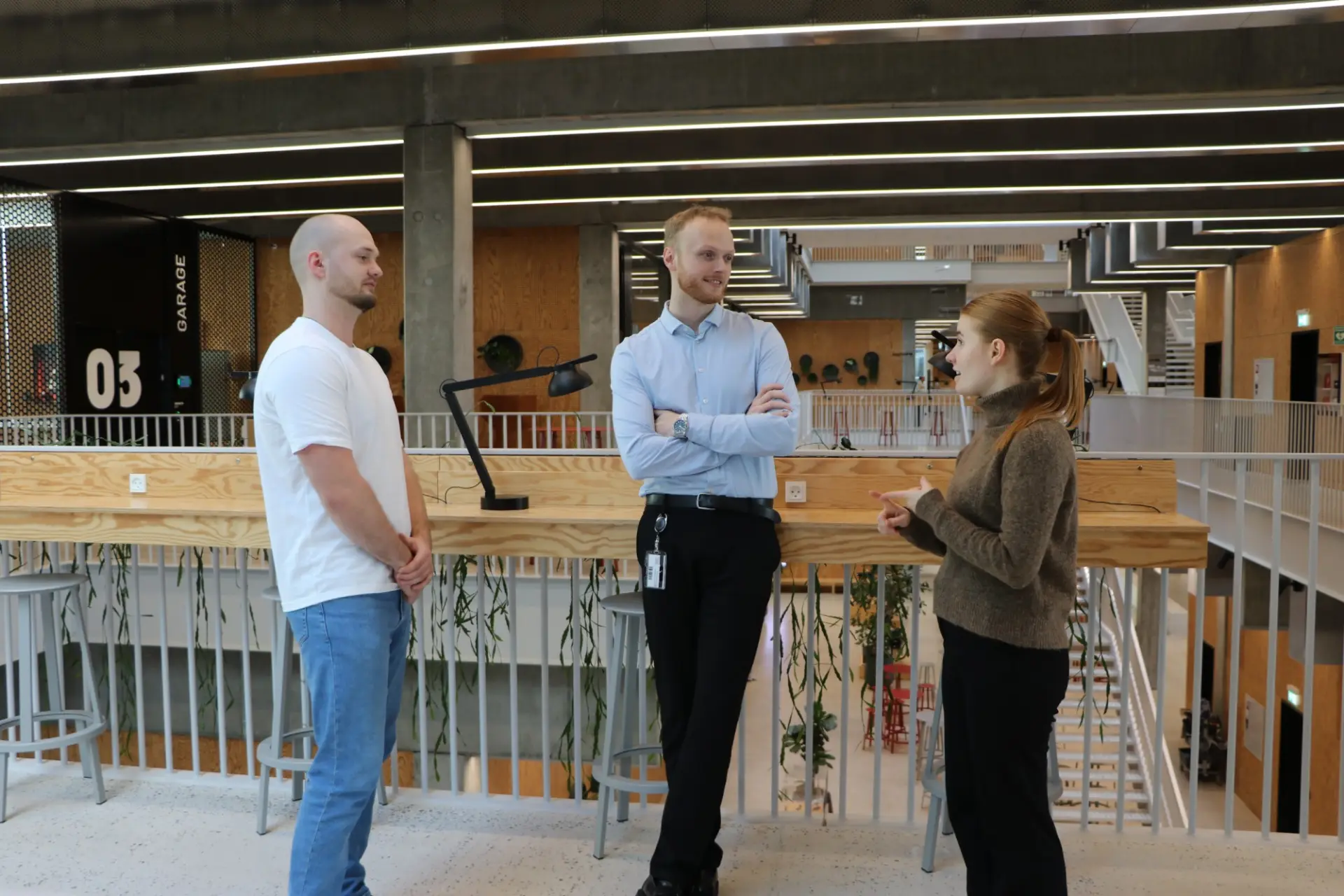 Three people from TrailBlaze talking on a walkway in a bright university building